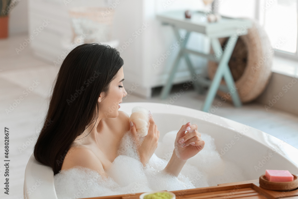 Relaxed young woman taking bath with loofah at home