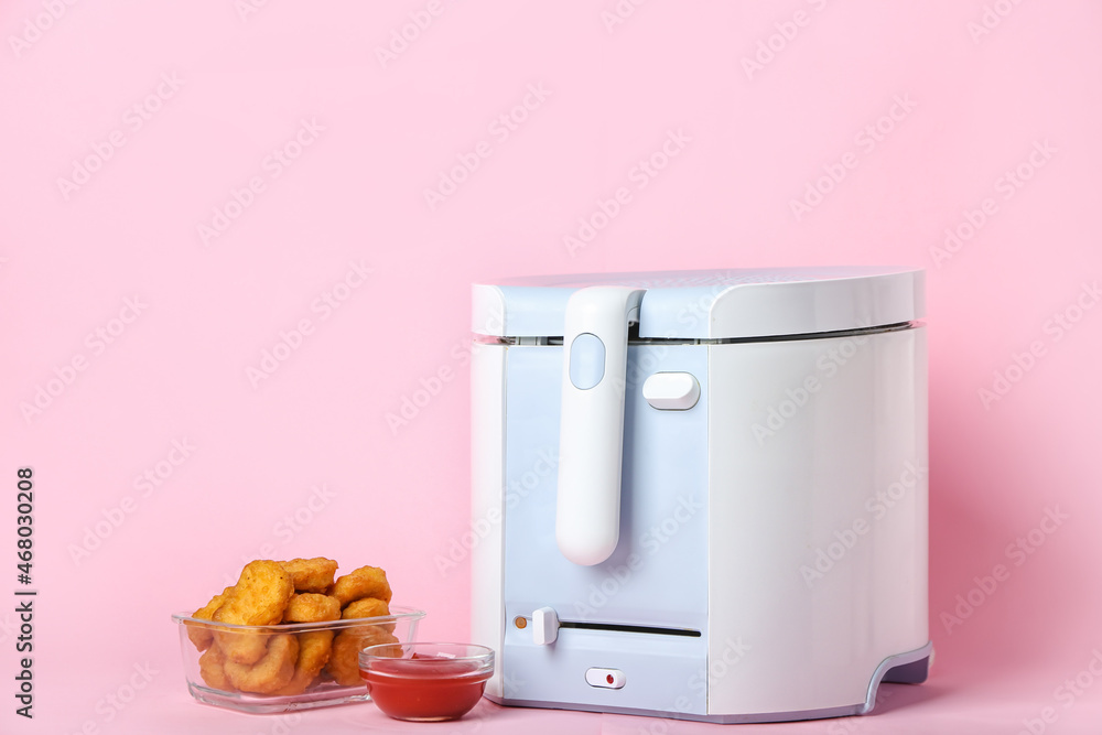 Modern deep fryer with nuggets and ketchup on color background