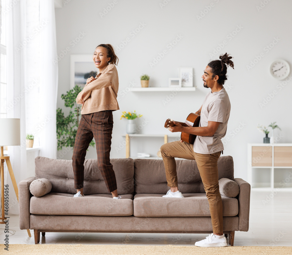 Young funny happy african american couple playing guitar and dancing at home on weekend