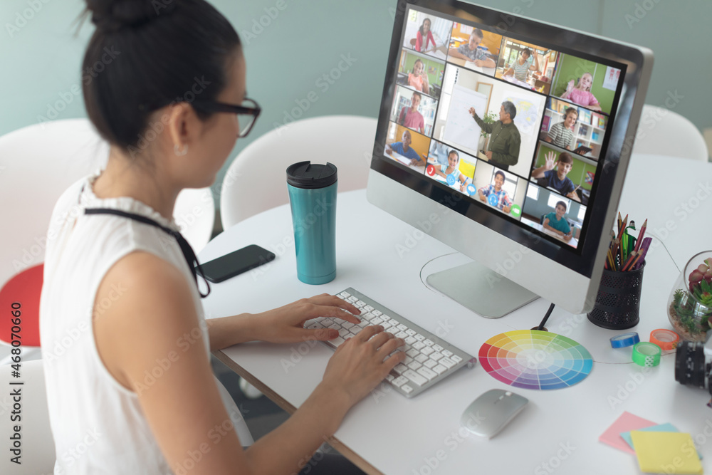 Caucasian girl using laptop for video call, with smiling diverse elementary school pupils on screen