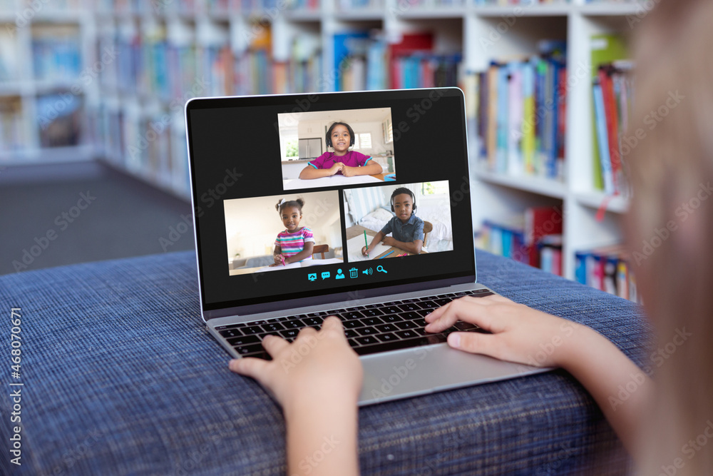 Caucasian girl using laptop for video call, with smiling diverse elementary school pupils on screen