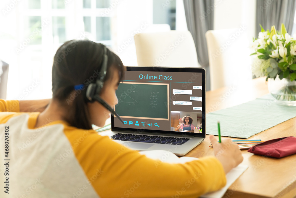 Asian girl using laptop for video call, with smiling female teacher on screen