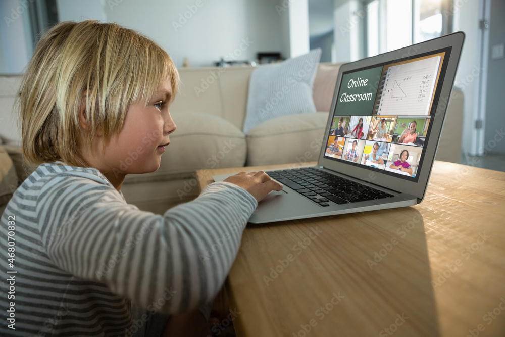 Caucasian boy using laptop for video call, with smiling diverse elementary school pupils on screen