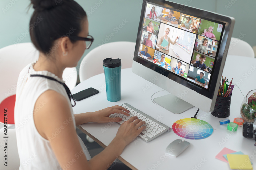 Caucasian girl using computer for video call, with diverse elementary school pupils on screen