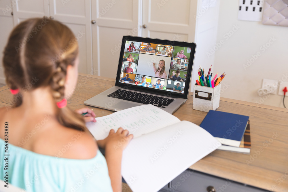 Caucasian girl using laptop for video call, with smiling diverse elementary school pupils on screen