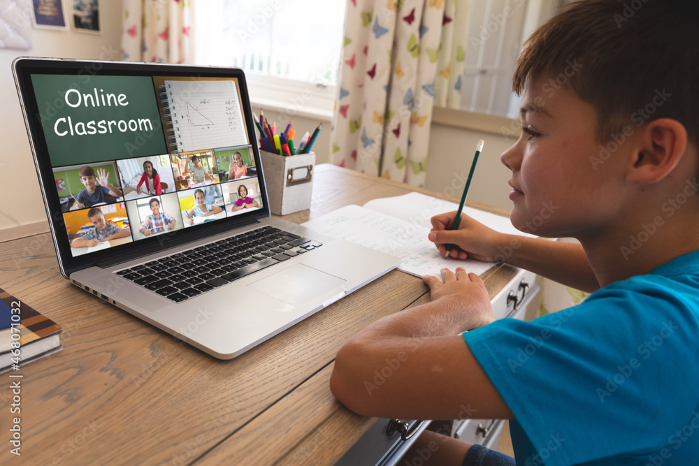 Caucasian boy using laptop for video call, with smiling diverse elementary school pupils on screen