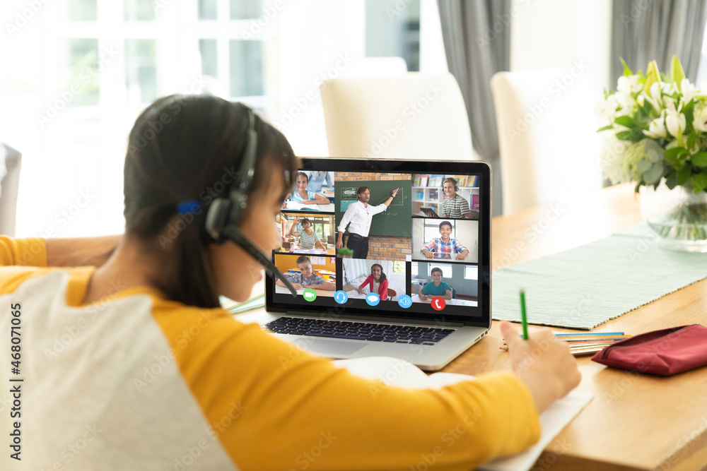 Asian girl using laptop for video call, with smiling diverse elementary school pupils on screen