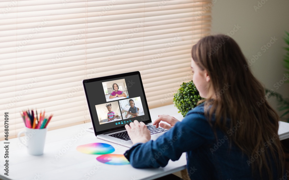 Caucasian girl using laptop for video call, with smiling diverse elementary school pupils on screen