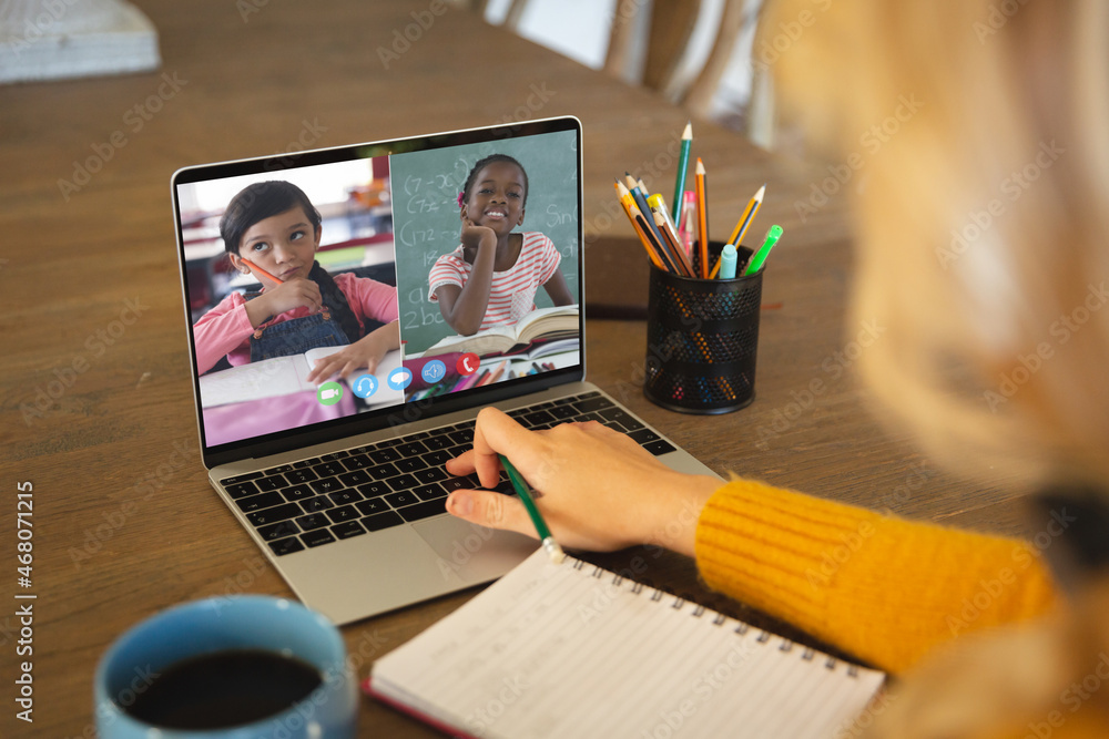 Caucasian woman using laptop for video call, with smiling diverse elementary school pupils on screen