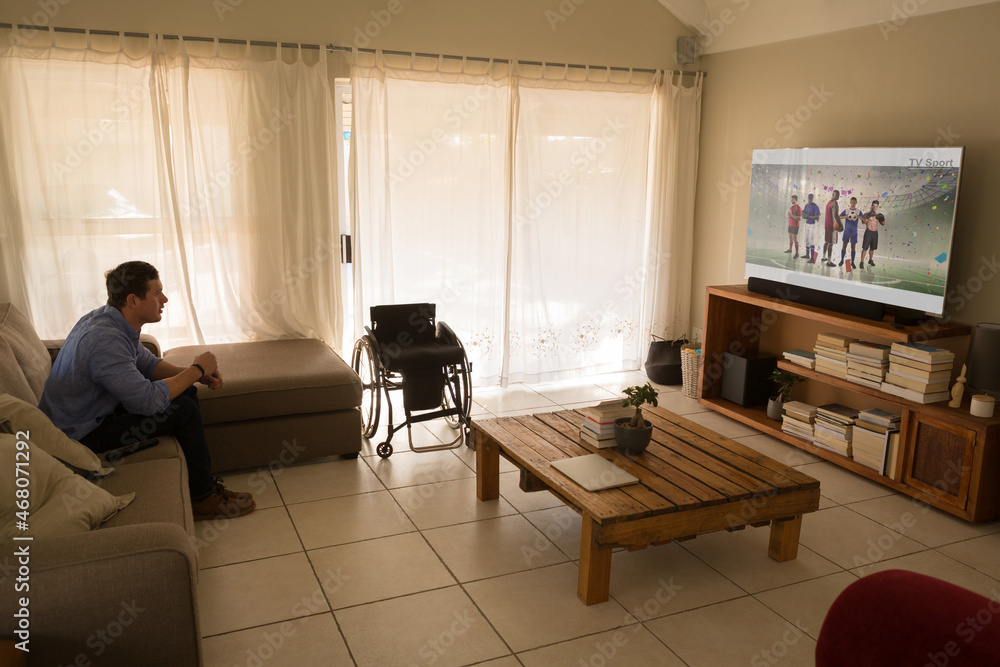 Caucasian disabled man sitting at home watching basketball match on tv