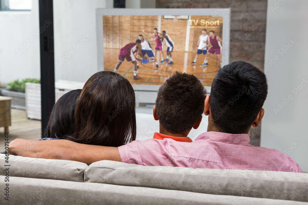 Rear view of family sitting at home together watching basketball match on tv