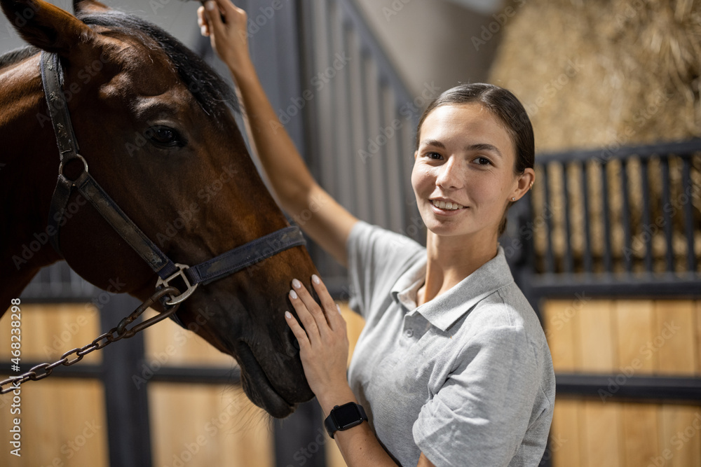 Portrait of female horseman with her brown Thoroughbred horse in stable. Concept of animal care. Rur