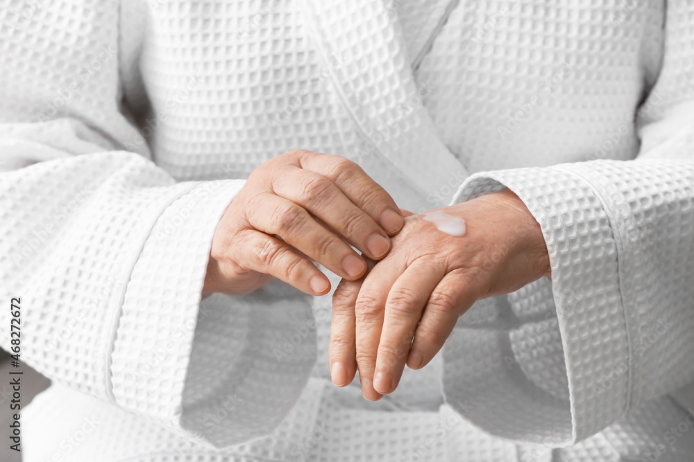 Elderly woman applying cosmetic cream onto her hands, closeup