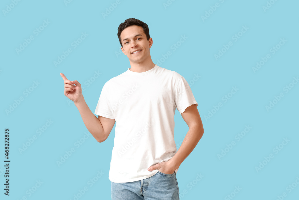 Handsome young man in stylish t-shirt pointing at something on color background