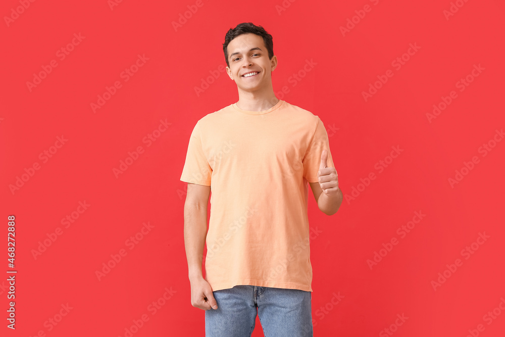 Handsome young man in stylish t-shirt showing thumb-up on color background