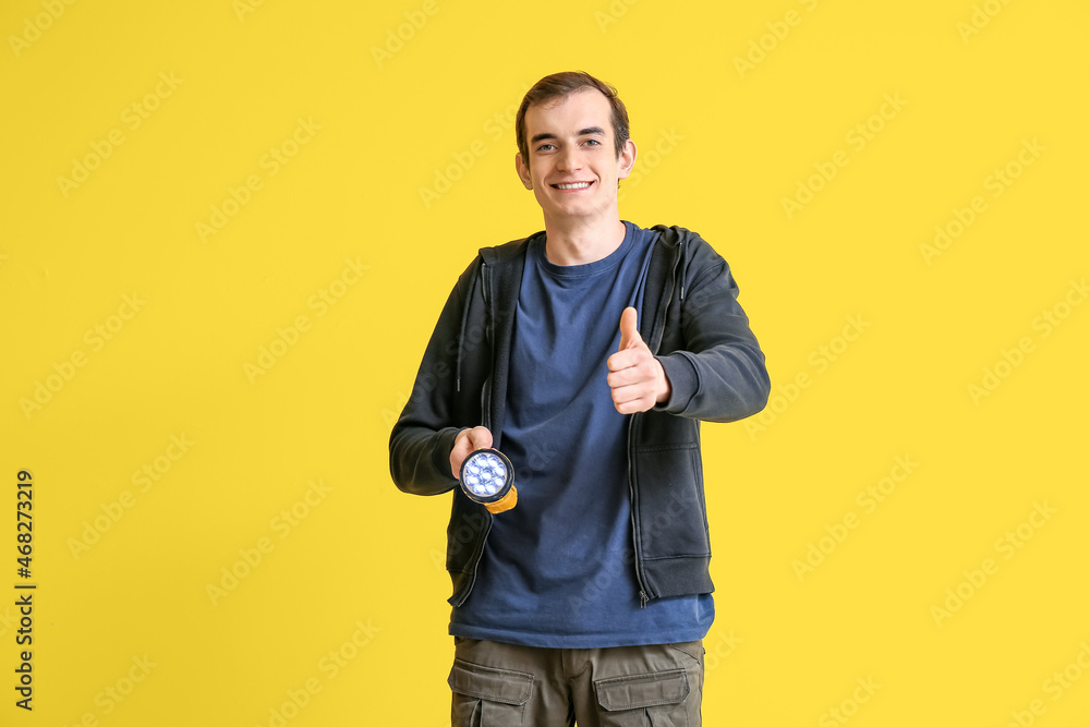 Young man with LED torch showing thumb-up on yellow background