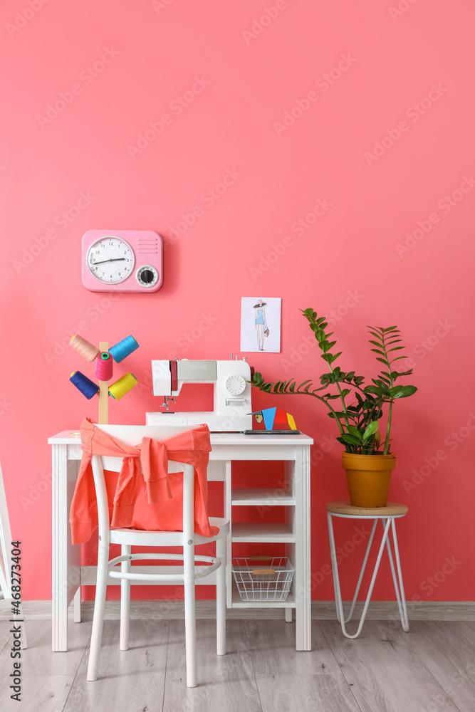 Modern tailors workplace with sewing machine and threads near pink wall