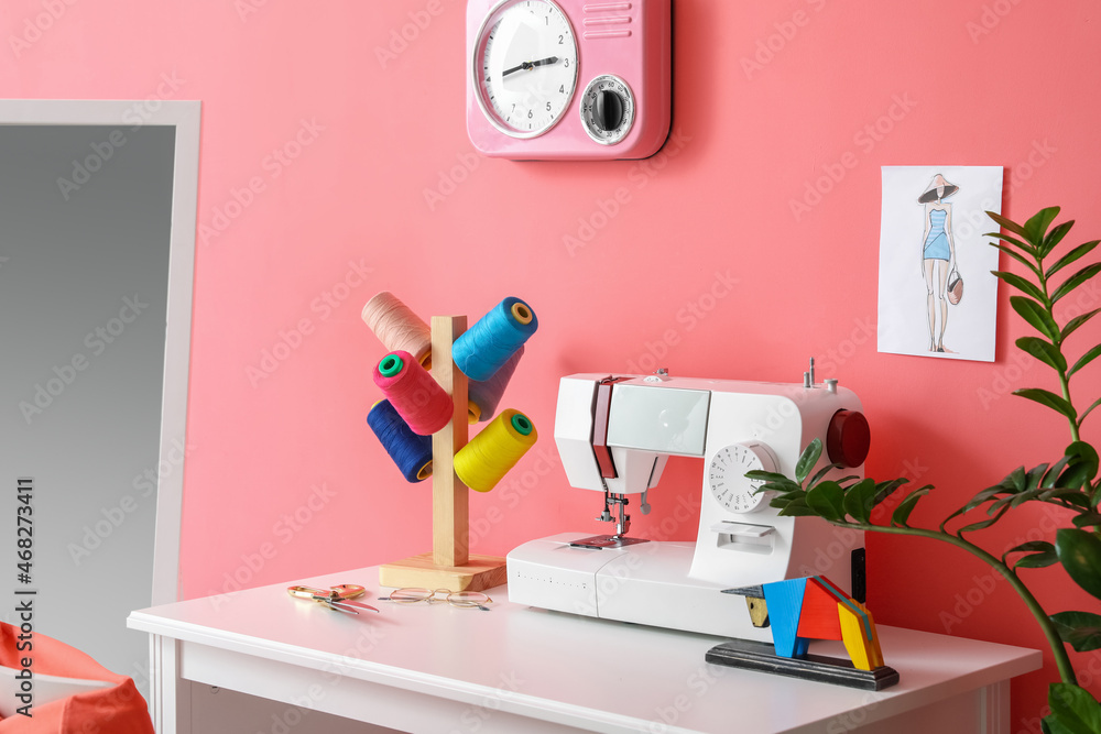 Modern tailors workplace with sewing machine and threads near pink wall