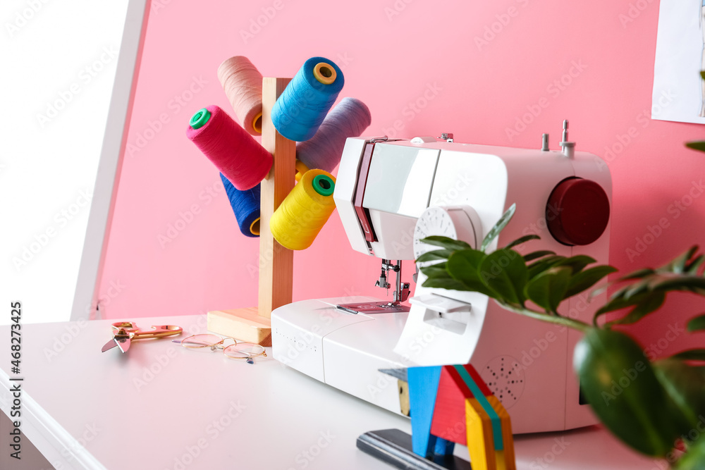 Modern tailors workplace with sewing machine and threads near pink wall