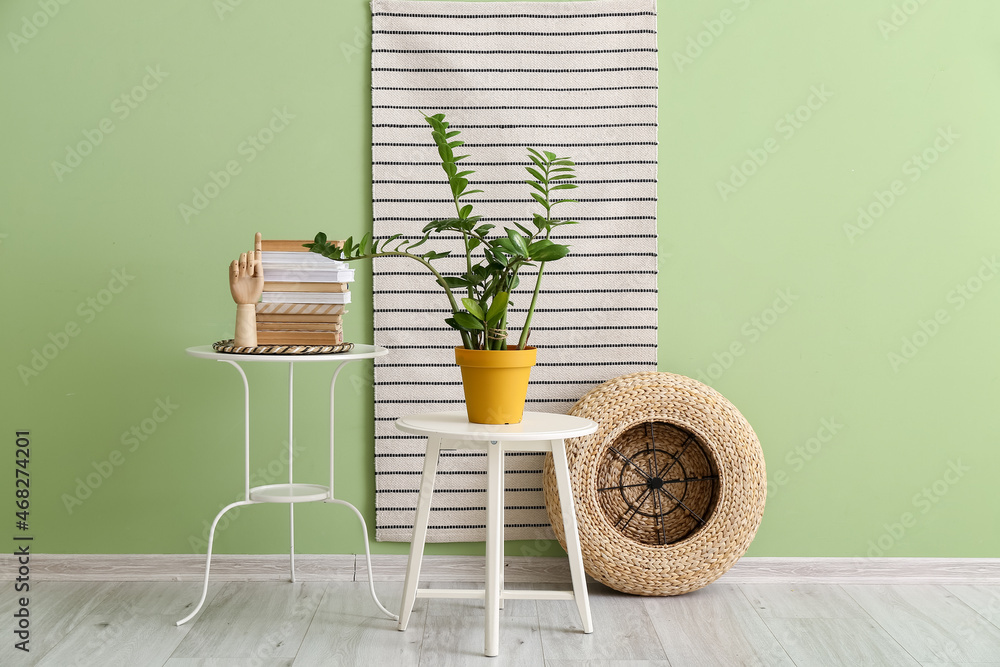 Wooden hand, books and plants on tables near color wall in room