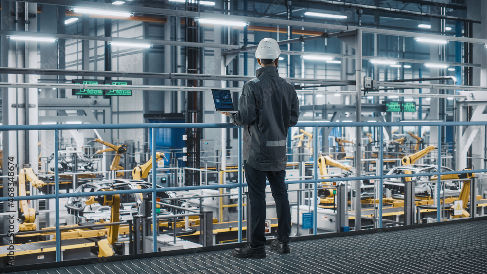 Car Factory Engineer in Work Uniform Using Laptop Computer. Automotive Industrial Manufacturing Faci