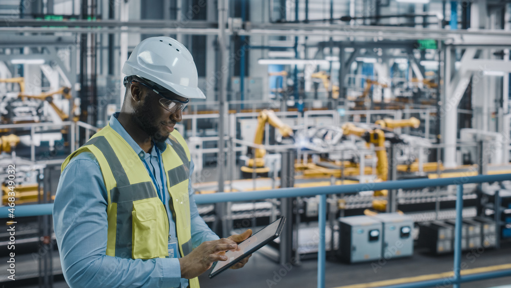 Happy African American Car Factory Engineer in High Visibility Vest Using Tablet Computer. Automotiv