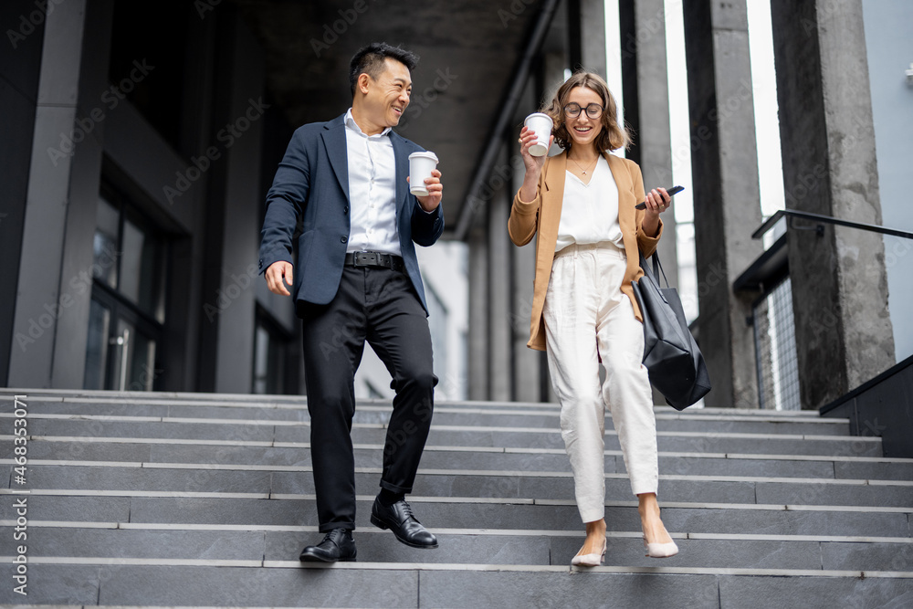 Asian businessman and caucasian businesswoman walking and talking on stairs in city. Concept of busi