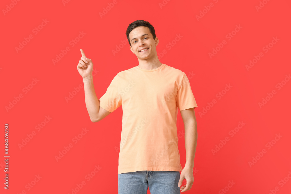 Handsome young man in stylish t-shirt pointing at something on color background