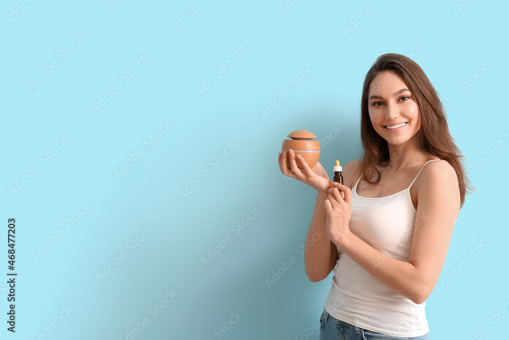 Beautiful smiling woman holding bottle with essential oil and diffuser on color background