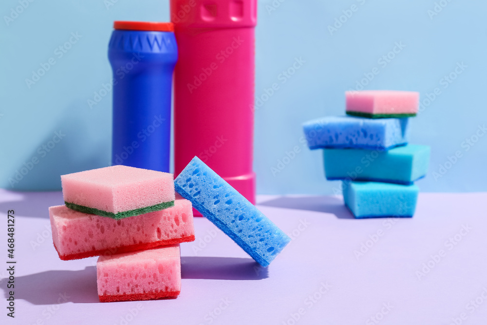 Cleaning sponges and bottles of detergent on color background