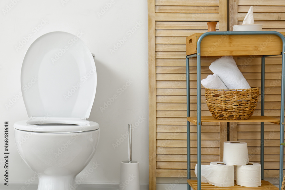 Interior of light restroom with toilet bowl and shelving unit