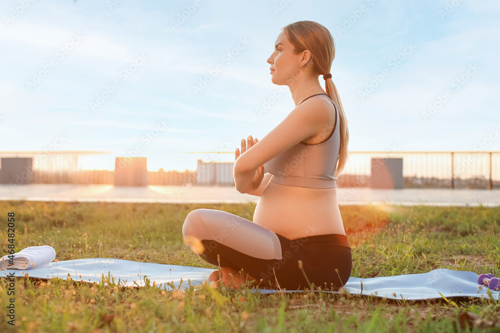 Young pregnant woman meditating in park