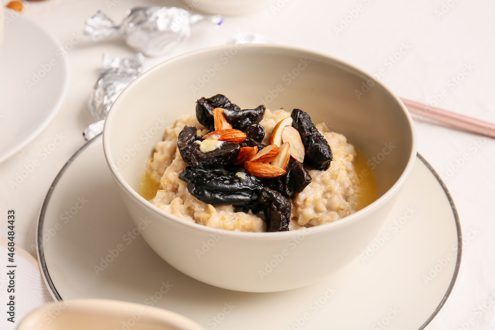 Tasty oatmeal with prunes and almond nuts in bowl on light table, closeup