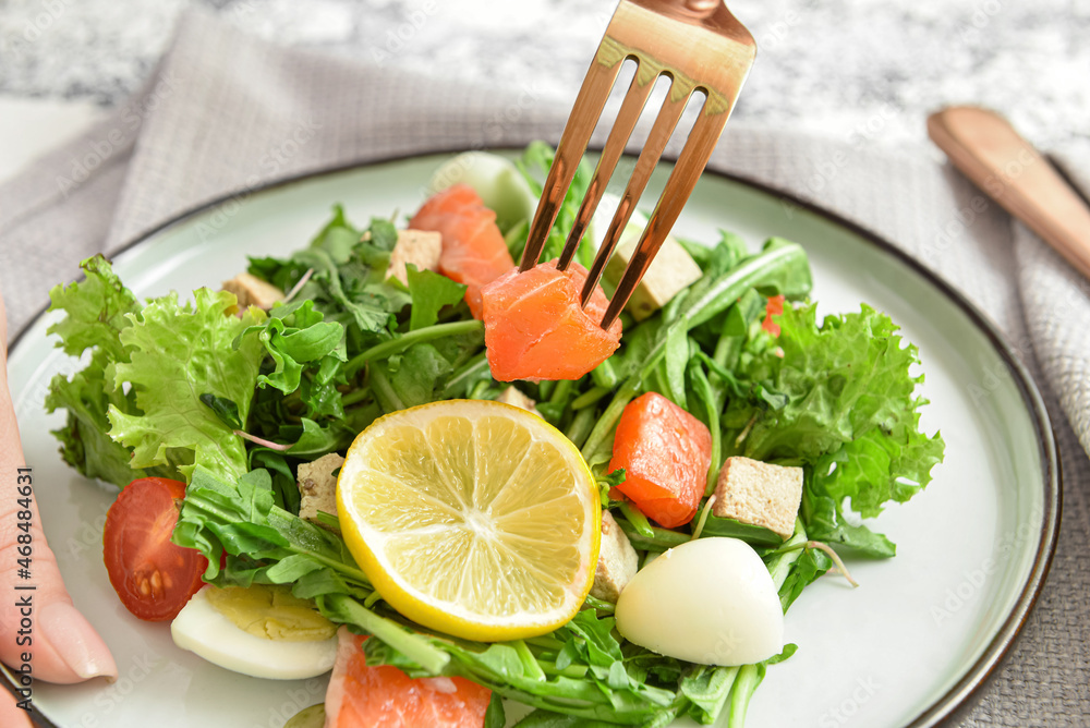 Woman eating fresh salad with salmon and vegetables at table, closeup