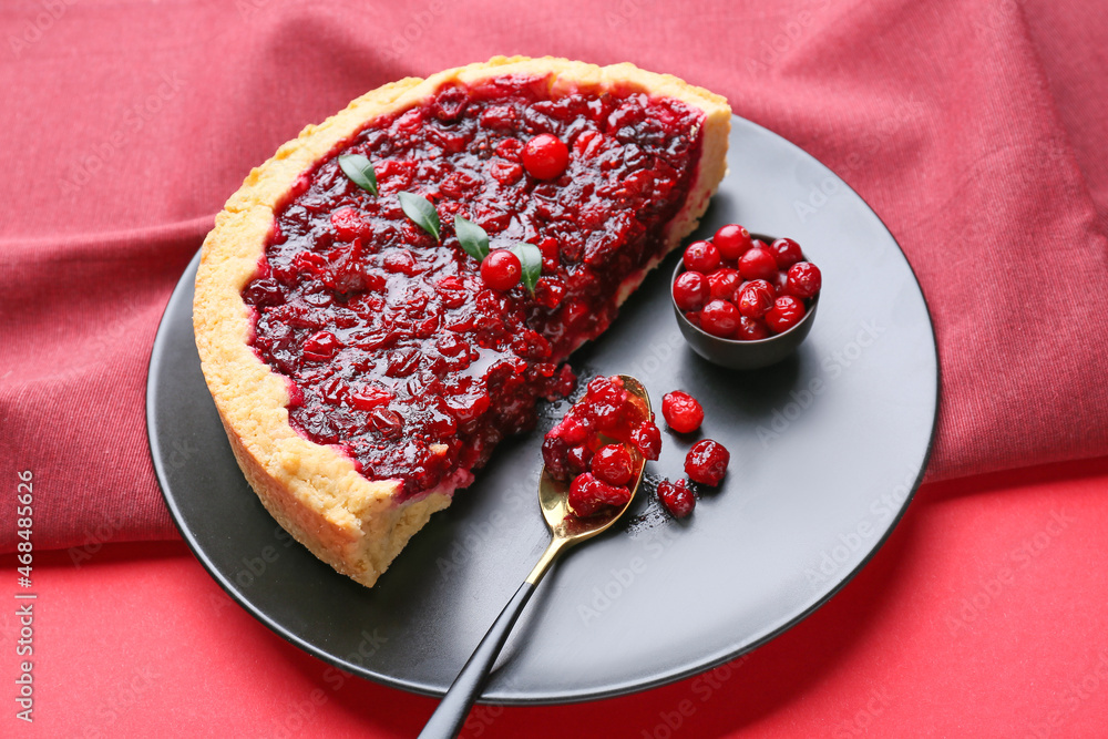 Plate with cut tasty lingonberry pie on color background