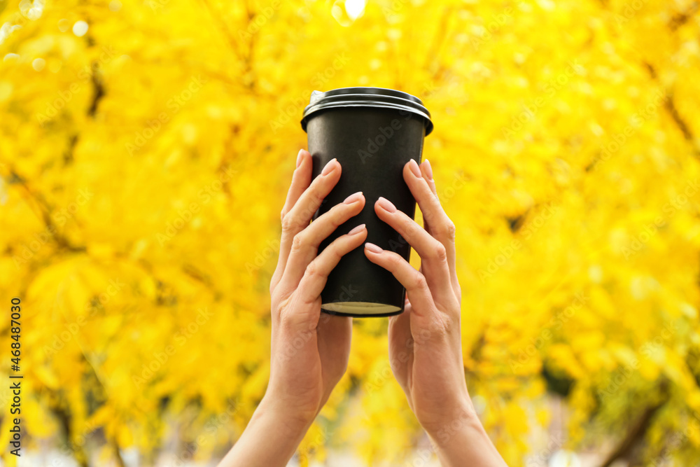 Woman holding takeaway cup of tasty coffee in autumn park