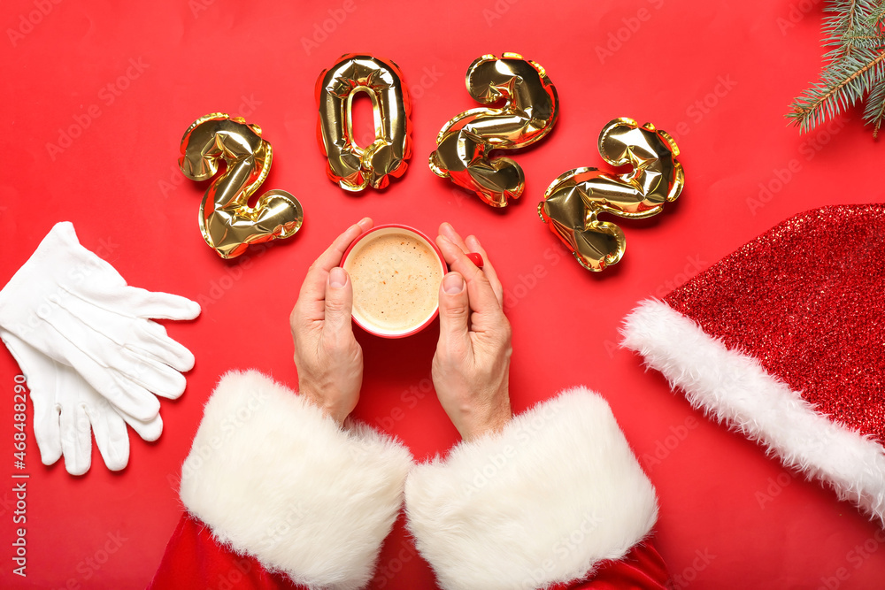 Santa Claus with cup of coffee and balloons in shape of figure 2022 on red background