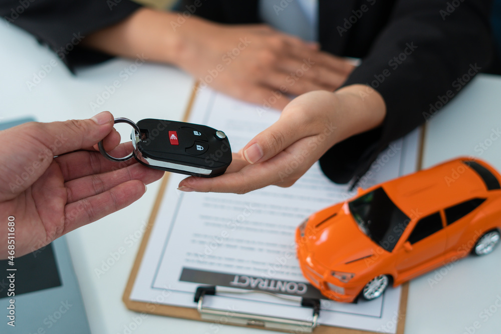 Close-up partial view of dealer giving car key to new owner