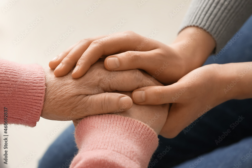 Young woman holding hands of grandmother at home, closeup