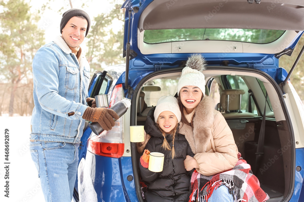 Happy family drinking hot tea in forest on winter day