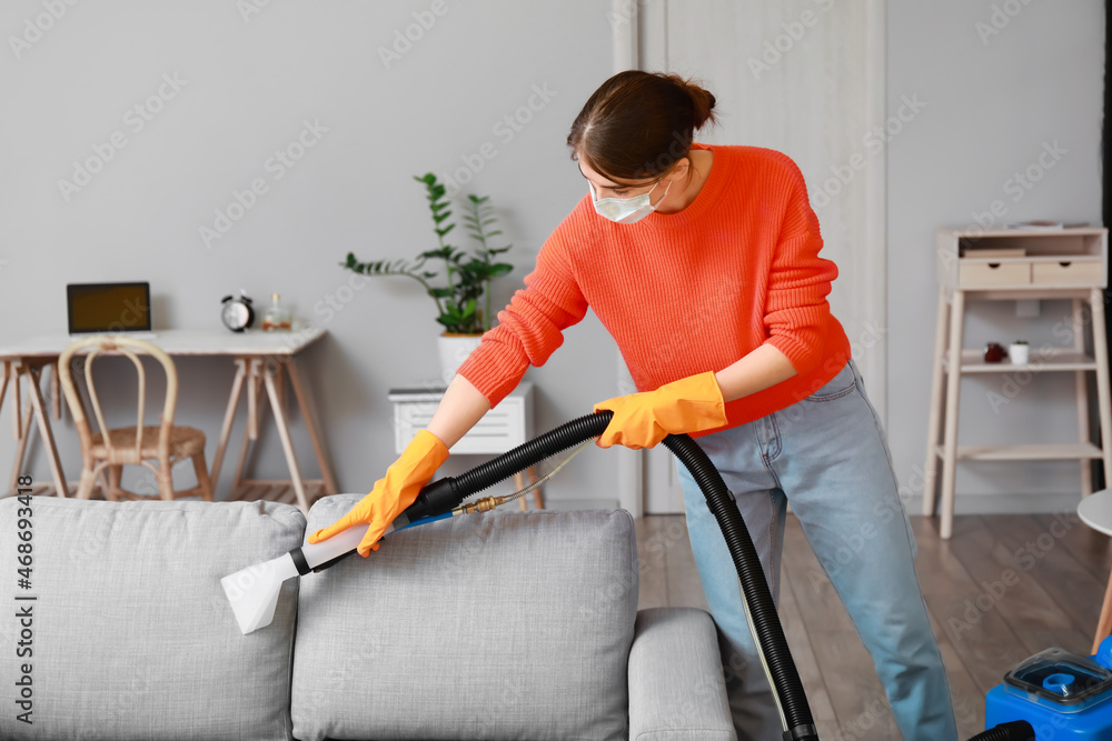 Woman removing dirt from grey sofa with vacuum cleaner in room