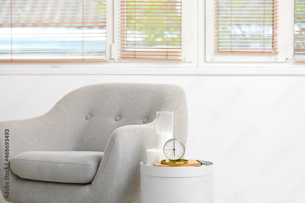 Stylish armchair and alarm clock on table in interior of room