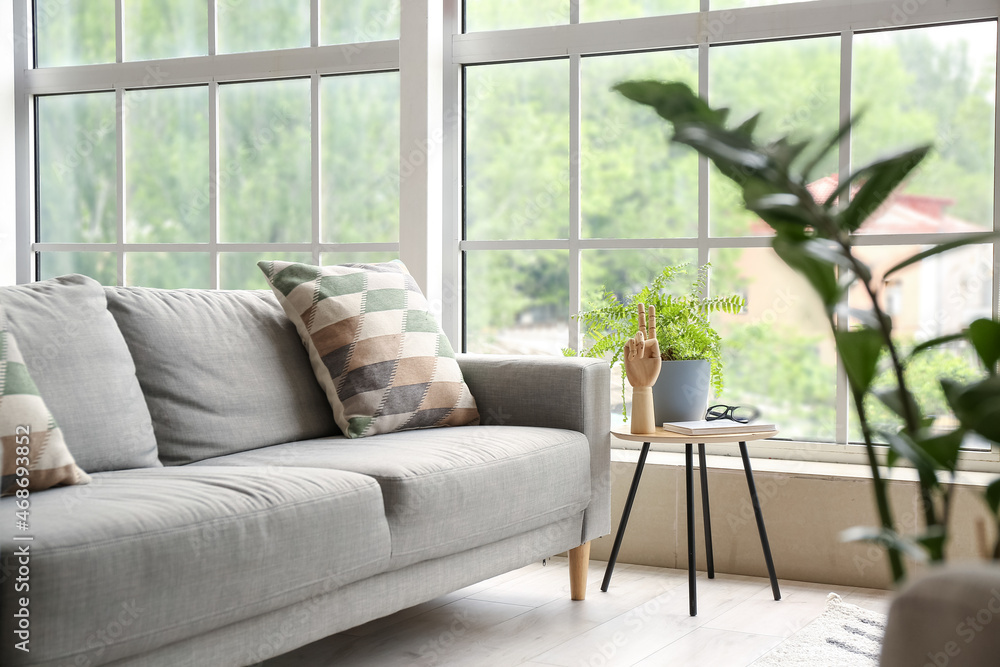 Comfortable sofa, table with wooden hand and houseplant in room with big window