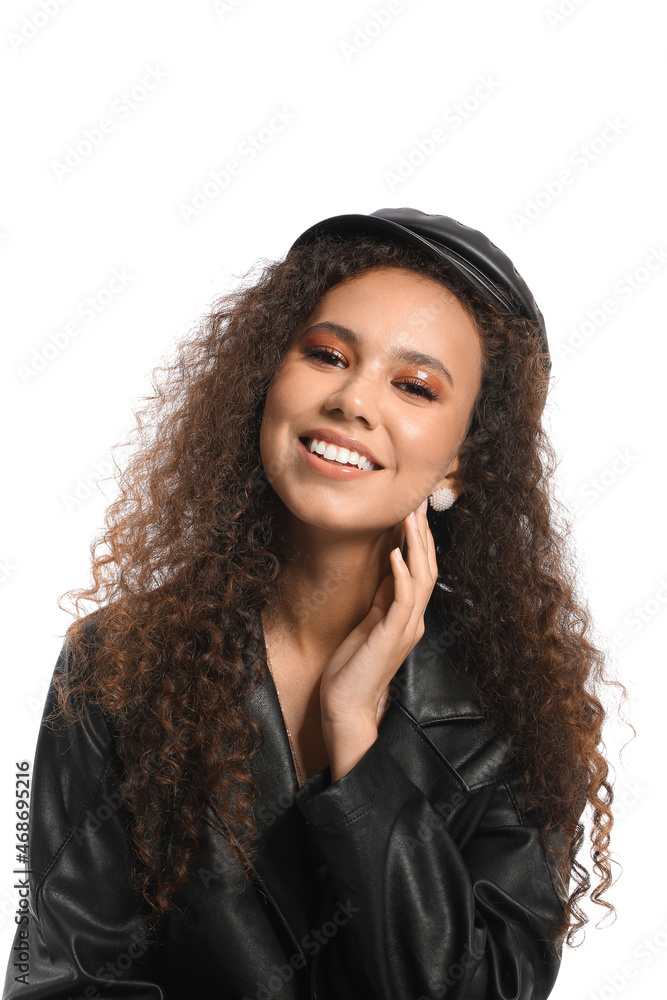 Beautiful African-American woman in stylish cap and leather jacket on white background