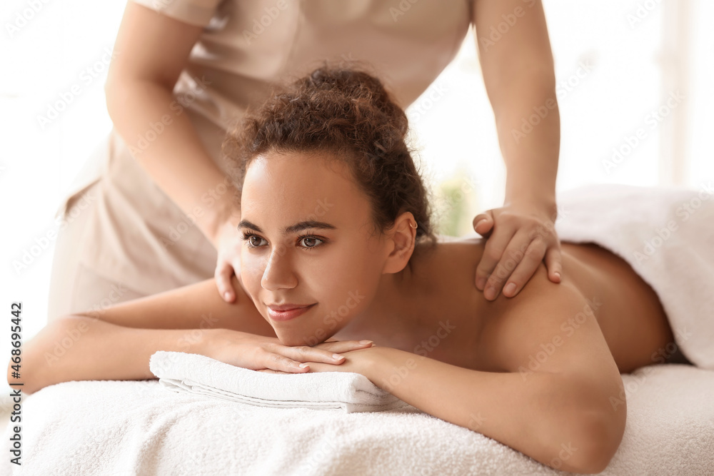 Beautiful African-American woman getting massage by therapist in spa salon