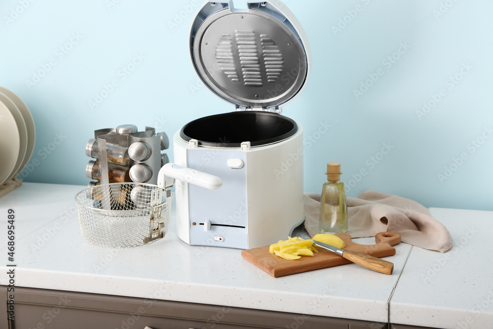 Wooden board with sliced potatoes and new deep fryer on kitchen table