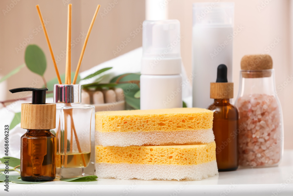 Bath sponges, bottles of cosmetic products and reed diffuser on table