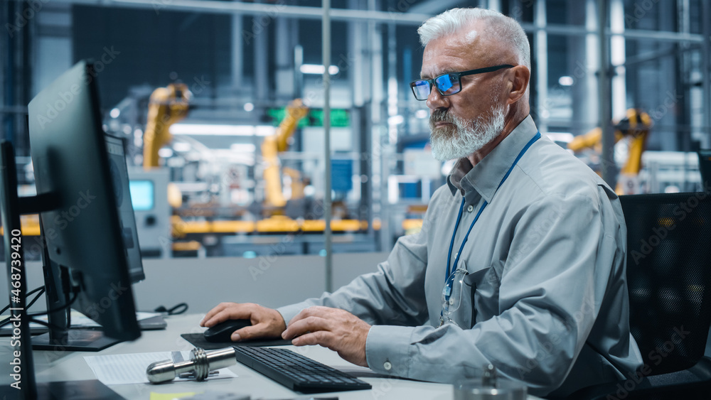 Car Factory Office: Portrait of Male Engineer Working on Computer. Automated Robot Arm Assembly Line