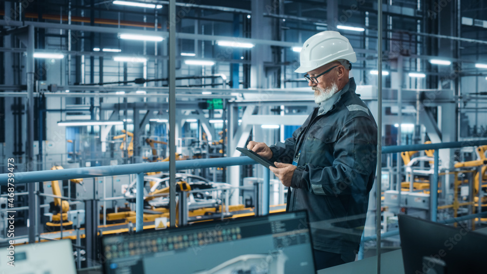 Car Factory: Male Automotive Engineer Wearing Hard Hat, Standing Using Tablet Computer. Monitoring, 