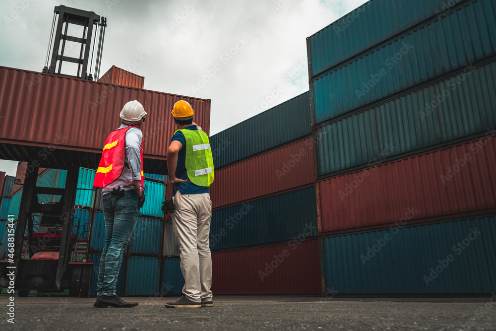 Industrial worker works with co-worker at overseas shipping container yard . Logistics supply chain 